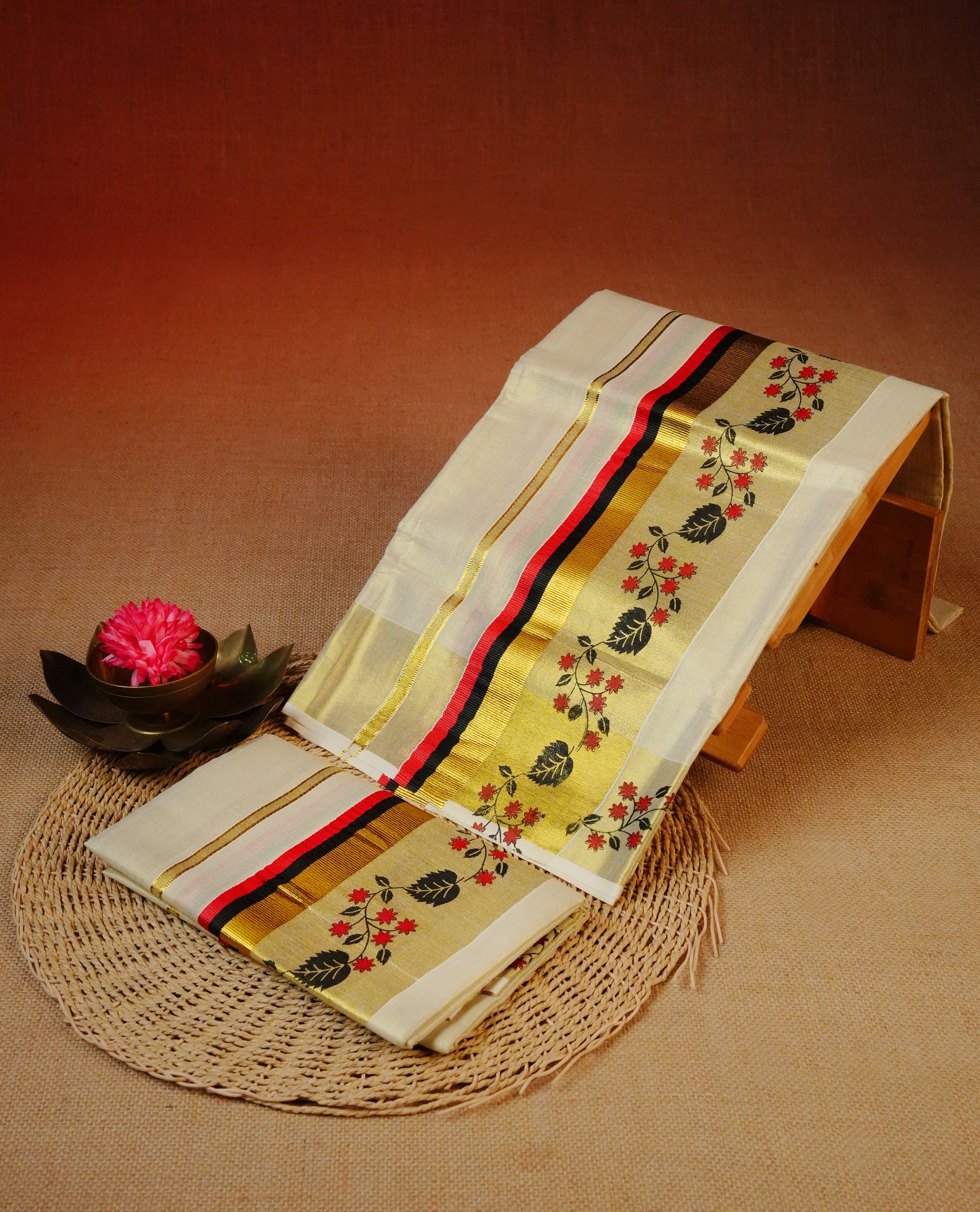 Cream Colour tissue set mundu featuring a plain body, enhanced with delicate red floral vine motifs & Black, Red & a gold zari kara.