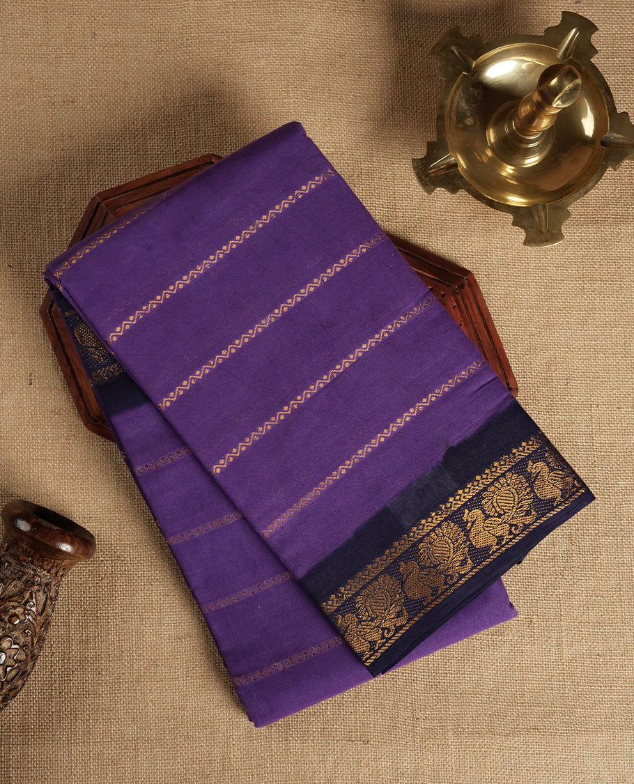 Purple colour Chettinad cotton saree adorned with subtle golden zari stripes all over, The contrast black border features intricate peacock and floral motifs & Comes with a matching blouse piece.