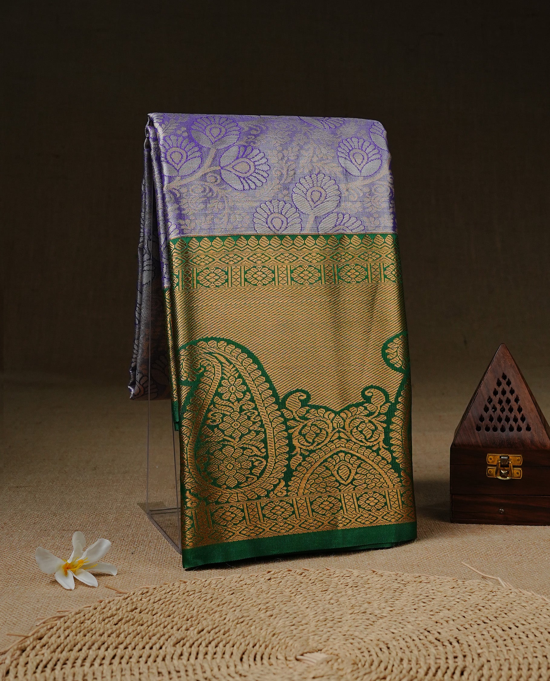 Light purple colour tissue saree featuring silver & gold zari floral kodi pattern on the body, highlighted by a contrast Green colour border with gold traditional zari, paired with a matching blouse piece.