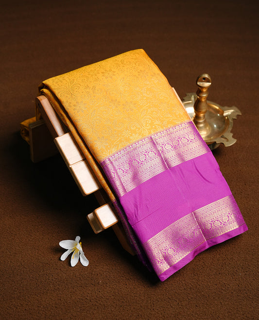 Yellow colour semi wedding saree featuring gold zari floral kode pattern on body, contrast Purple colour with traditional border, paired with matching blouse piece.