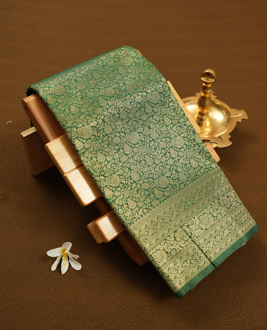 Green colour semi silk brocade saree featuring intricate Gold Floral kodi patterns across the body, complemented by a rich self colour woven border and pallu, paired with a matching blouse.