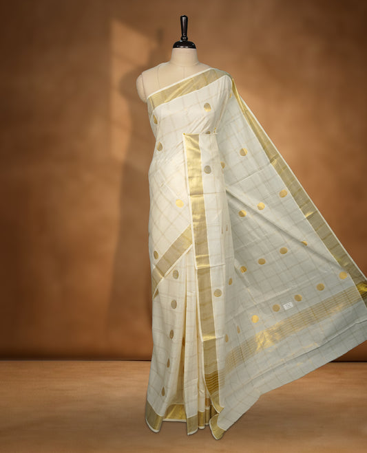 Elegant Off white colour cotton Kerala saree with gold zari check stripes and buttas, broad kasavu border, and richly woven traditional pallu, paired with a matching blouse
