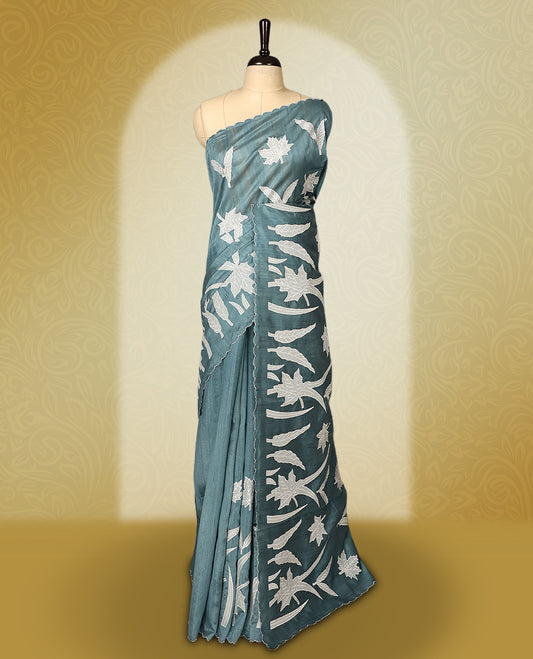 Teal colour semi tussar saree adorned with elegant white applique work in leaf and floral designs across the body and border, paired with a matching blouse.