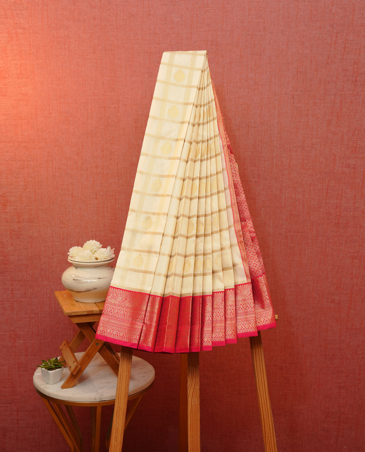 Cream colour soft silk saree featuring gold zari checks with floral mottifs on body, contrast reddish pink colour gold zari pecock traditional border, grand pallu comes with matching blouse piece.