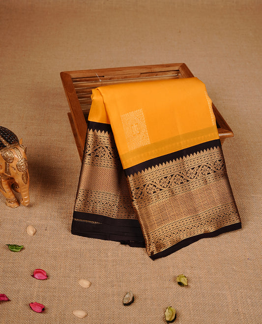 Mustard colour traditional kancheepuram silk saree featuring gold zari motifs on body, complemented by contrast black colour with gold zari traditional border, paired with matching blouse piece.