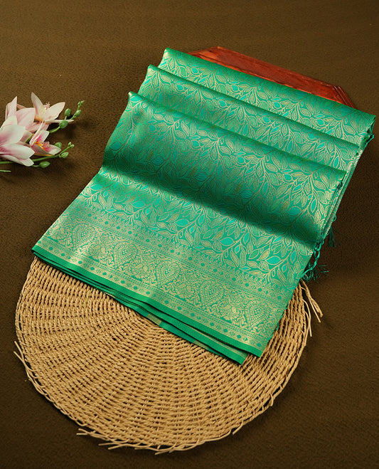 Green colour semi soft silk saree featuring an all-over woven leaf pattern in gold colour, finished with a matching border adorned with detailed paisley and floral motifs, and a matching blouse piece.