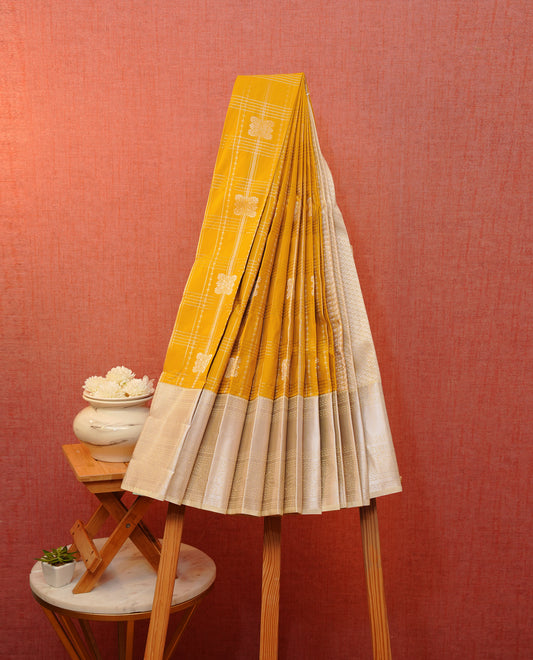 Mustard yellow colour soft silk saree featuring gold zari checks with floral mottifs on body, contrast cream colour gold zari traditional border, grand pallu comes with matching blouse piece.