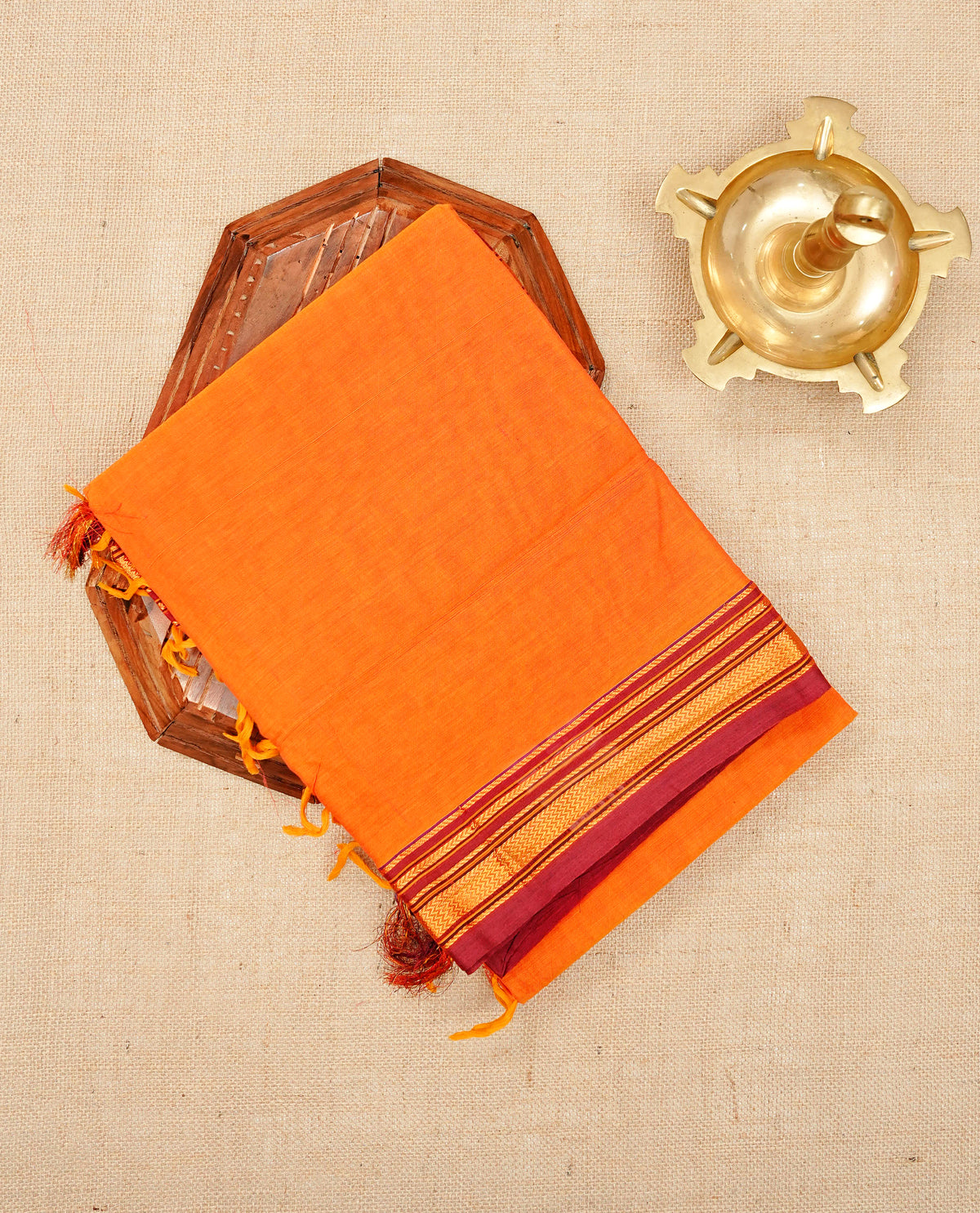 Orange colour Narayanapattu cotton saree with a plain body, complemented by a Maroon colour with elegant gold zari detailing border & contrast striped pallu, paired with a matching blouse piece.