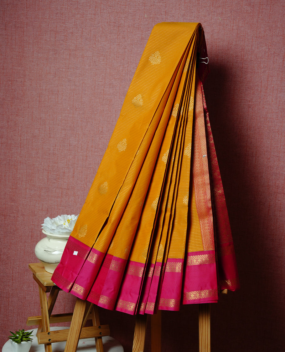 Mustard coloured soft silk saree featuring gold zari stripes and motifs across the body, enhanced with a contrast rani pink border and pallu, paired with a matching contrast blouse piece.