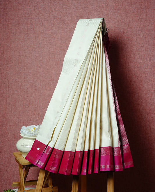 Cream coloured soft silk saree featuring gold zari stripes and motifs across the body, enhanced with a contrast Magenta border and pallu, paired with a matching contrast blouse piece.