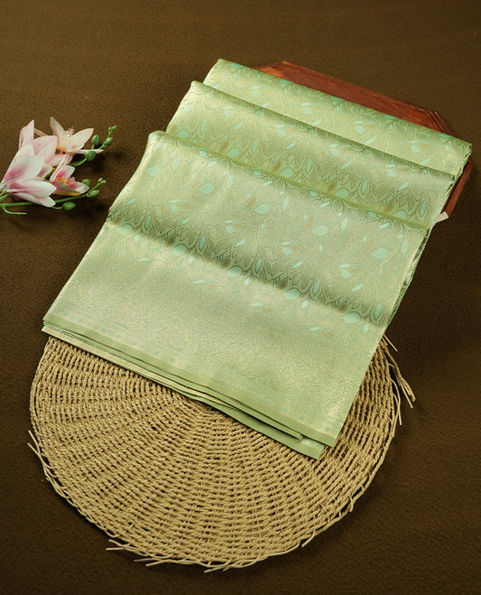 Light Green colour semi soft silk saree featuring an all-over woven leaf pattern in gold colour, finished with a matching border adorned with detailed paisley and floral motifs, and a matching blouse piece.