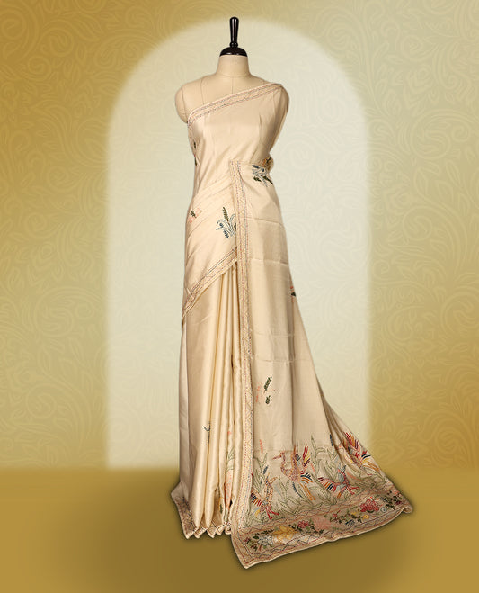 Cream colour pure tussar saree adorned with delicate Peach and green floral embroidery along the border and scattered motifs across the body, paired with a matching blouse.