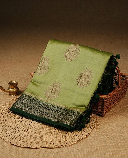 Pastel Pistachio Green Colour Tussar Silk saree with elegant antique zari floral motifs On Body, a contrasting dark green zari border, a rich zari pallu, and a matching blouse piece.