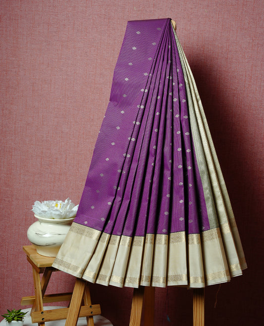Purple coloured soft silk saree featuring gold zari stripes and motifs across the body, enhanced with a contrast Cream border and pallu, paired with a matching contrast blouse piece.