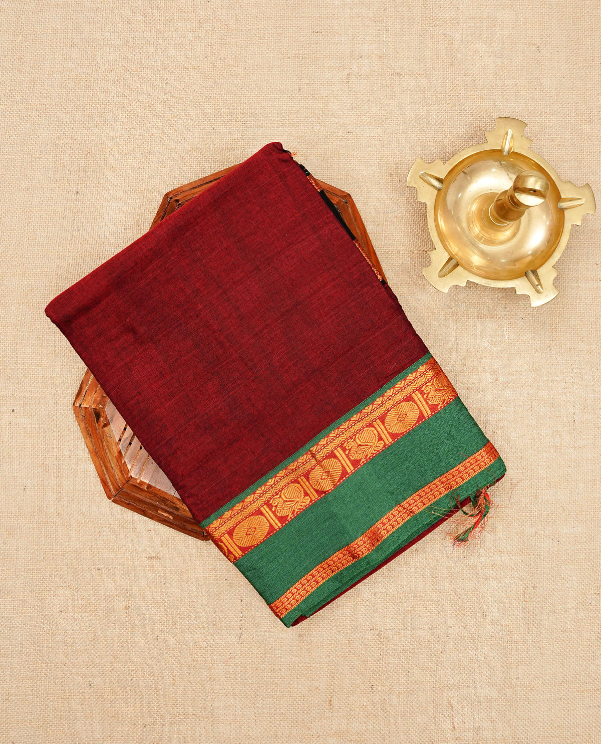 Dark Red colour Narayanapattu cotton saree with a plain body, complemented by a Green Colour with Gold zari border & contrast pallu, paired with a matching blouse piece.