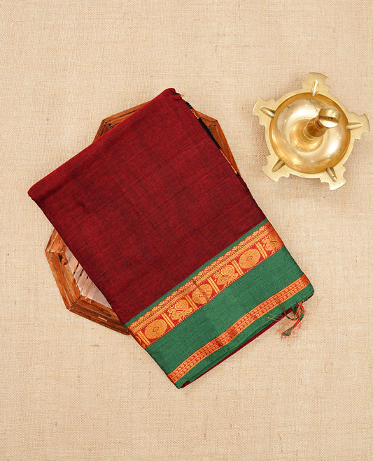 Dark Red colour Narayanapattu cotton saree with a plain body, complemented by a Green Colour with Gold zari border & contrast pallu, paired with a matching blouse piece.