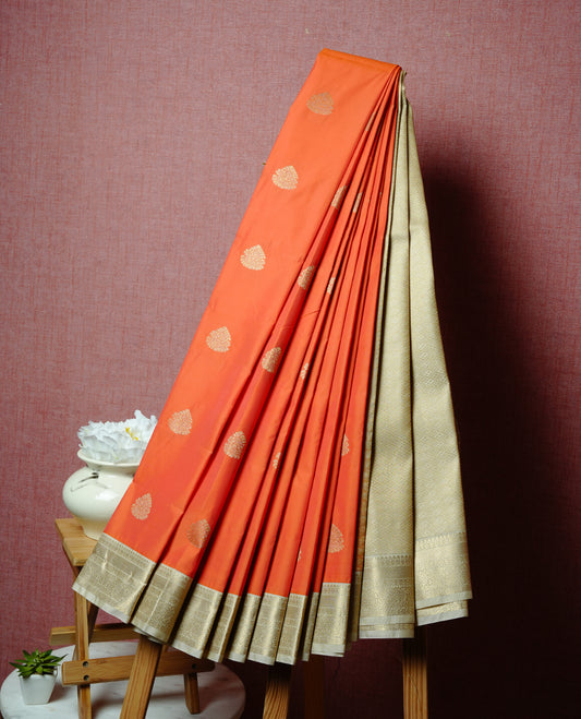 Orange coloured soft silk saree featuring gold zari motifs across the body, enhanced with a contrast Cream border and pallu, paired with a matching contrast blouse piece.