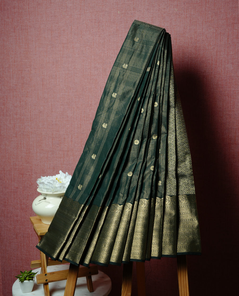 Dark green coloured soft silk saree featuring gold zari stripes and motifs across the body, enhanced with selfcolour border and pallu, paired with a matching blouse piece.