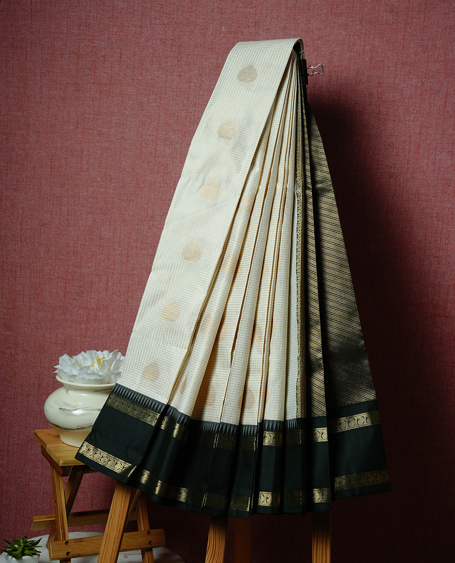 Cream coloured soft silk saree featuring gold zari stripes and motifs across the body, enhanced with a contrast Deep green border and pallu, paired with a matching contrast blouse piece