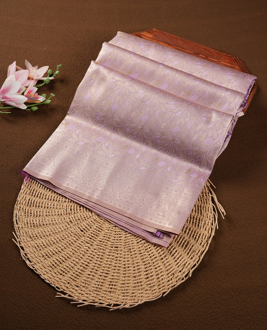 Lavender colour semi soft silk saree featuring an all-over woven leaf pattern in gold colour , finished with a matching border adorned with detailed paisley and floral motifs, and a matching blouse piece.