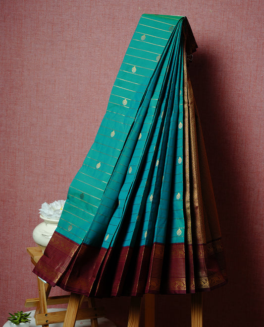 Green coloured soft silk saree featuring gold zari stripes and motifs across the body, enhanced with a contrast Maroon border and pallu, paired with a matching contrast blouse piece.