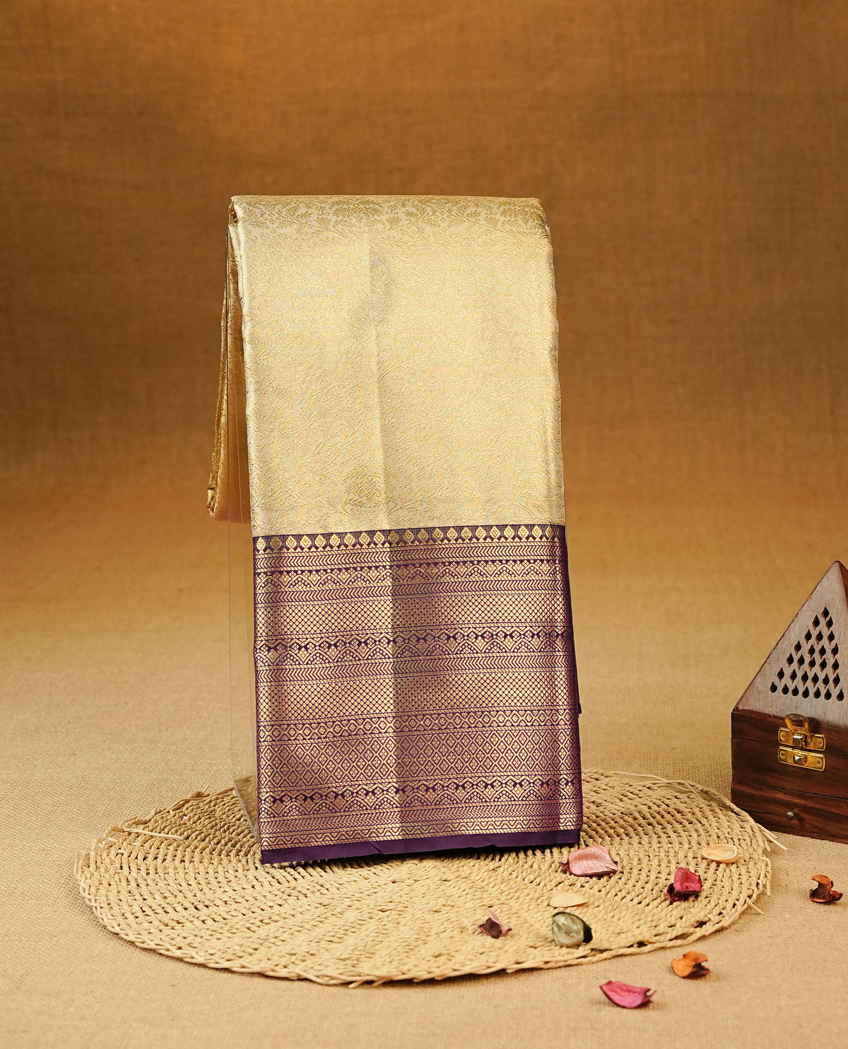 Beige colour Semi Tissue Silk Saree featuring gold zari Works on the body, complemented by an intricately woven gold zari pallu, a rich Purple border with gold zari work and paired with a matching plain blouse piece.