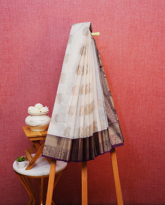 Off white colour silk saree featuring gold zari mango motifs on body, contrast purple with gold zari traditional border, contrast grand pallu comes with matching blouse piece .