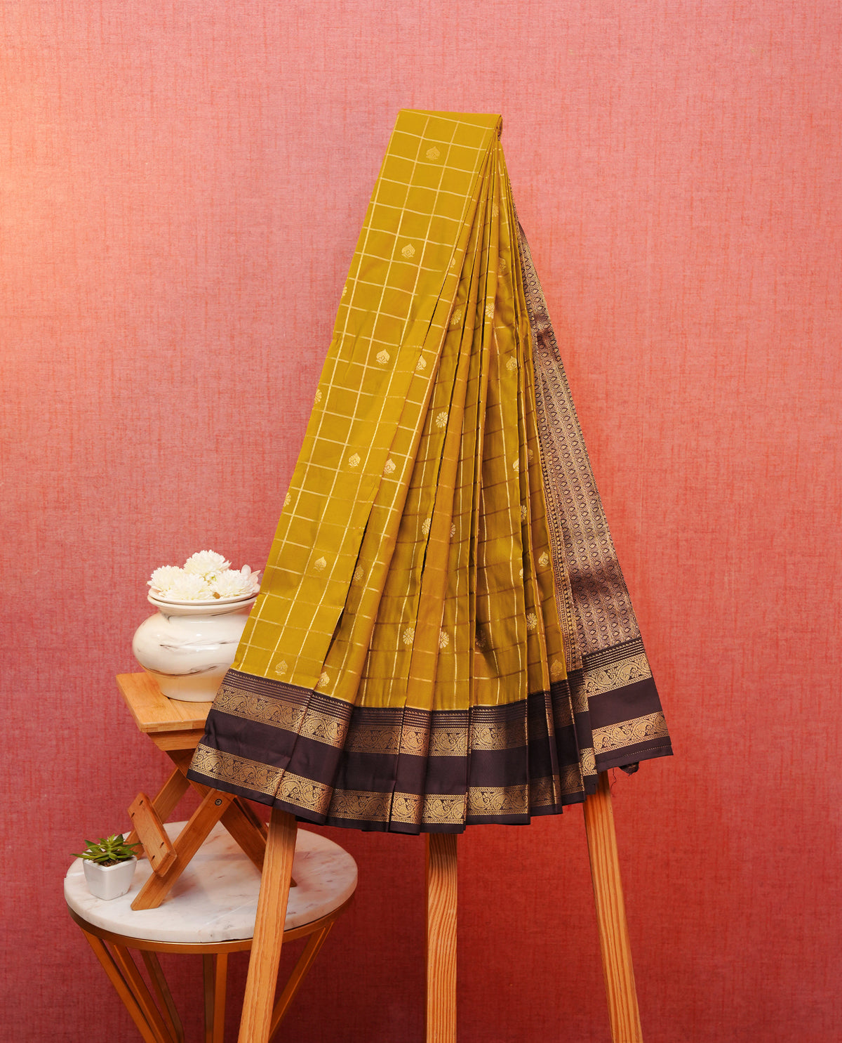 Dark mustard colour soft silk saree featuring floral gold zari checks with florals on body, contrast dark brown colour traditional border, grand pallu comes with matching blouse piece.