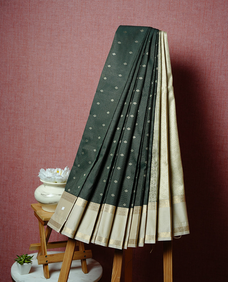 Dark green coloured soft silk saree featuring gold zari stripes and motifs across the body, enhanced with a contrast cream border and pallu, paired with a matching contrast blouse piece.
