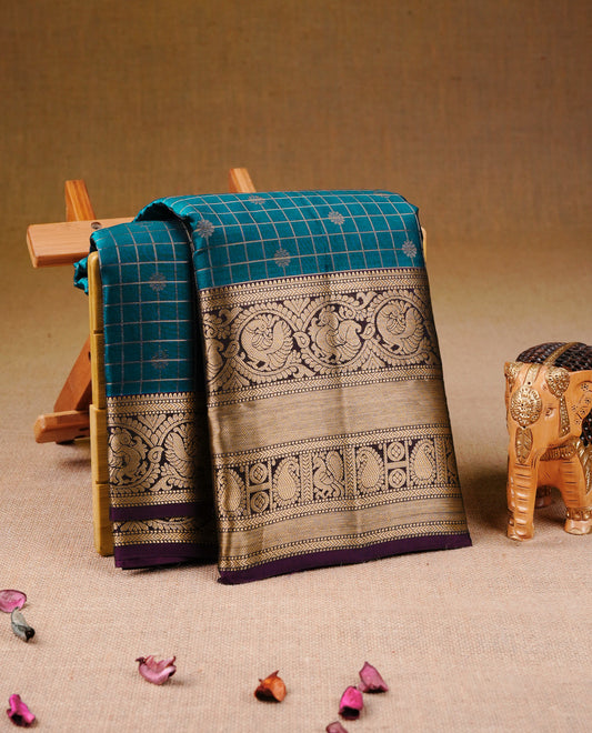 Teal Blue Colour Traditional Kancheepuram Silk Saree with Gold Zari Checks and Delicate Floral Buttas on the Body, Enhanced with a Contrast Purple Colour with Grand Gold Zari Traditional Border and Pallu, Paired with a Matching Blouse Piece.