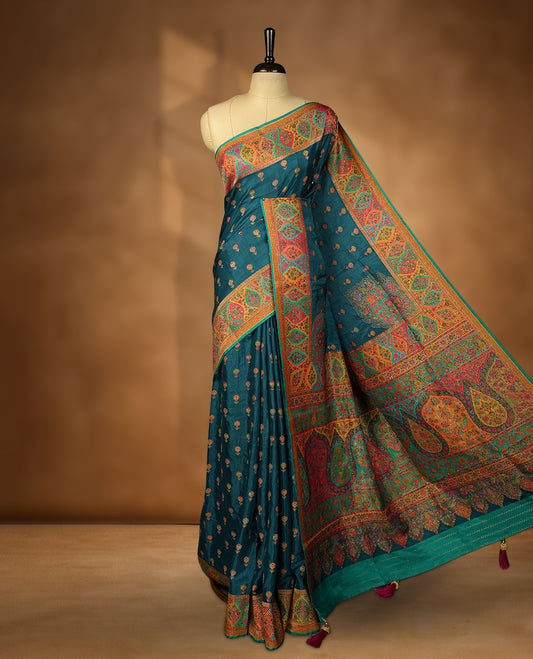 Dark teal blue colour Pashmina silk saree densely woven with intricate multicolour floral motifs across the body, framed by an opulent arabesque border and grand storytelling pallu, paired with a matching woven border blouse piece