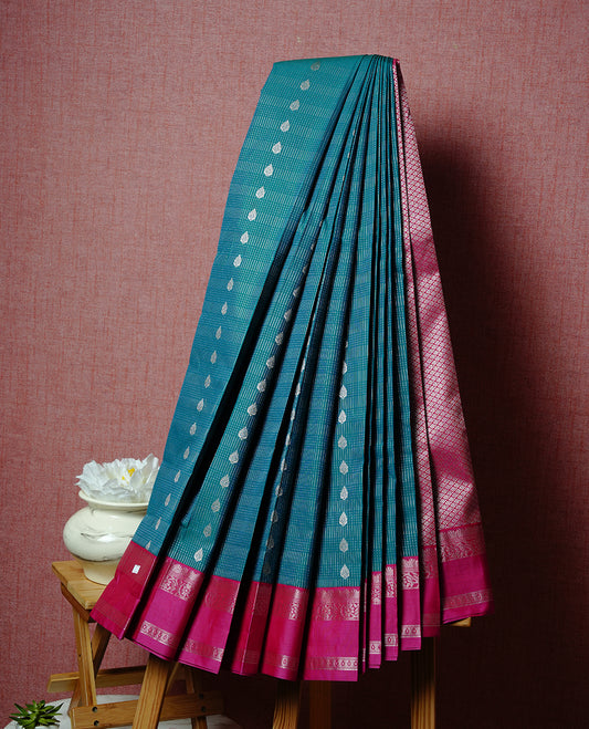 Teal coloured soft silk saree featuring gold zari stripes and motifs across the body, enhanced with a contrast Magenta border and pallu, paired with a matching contrast blouse piece.