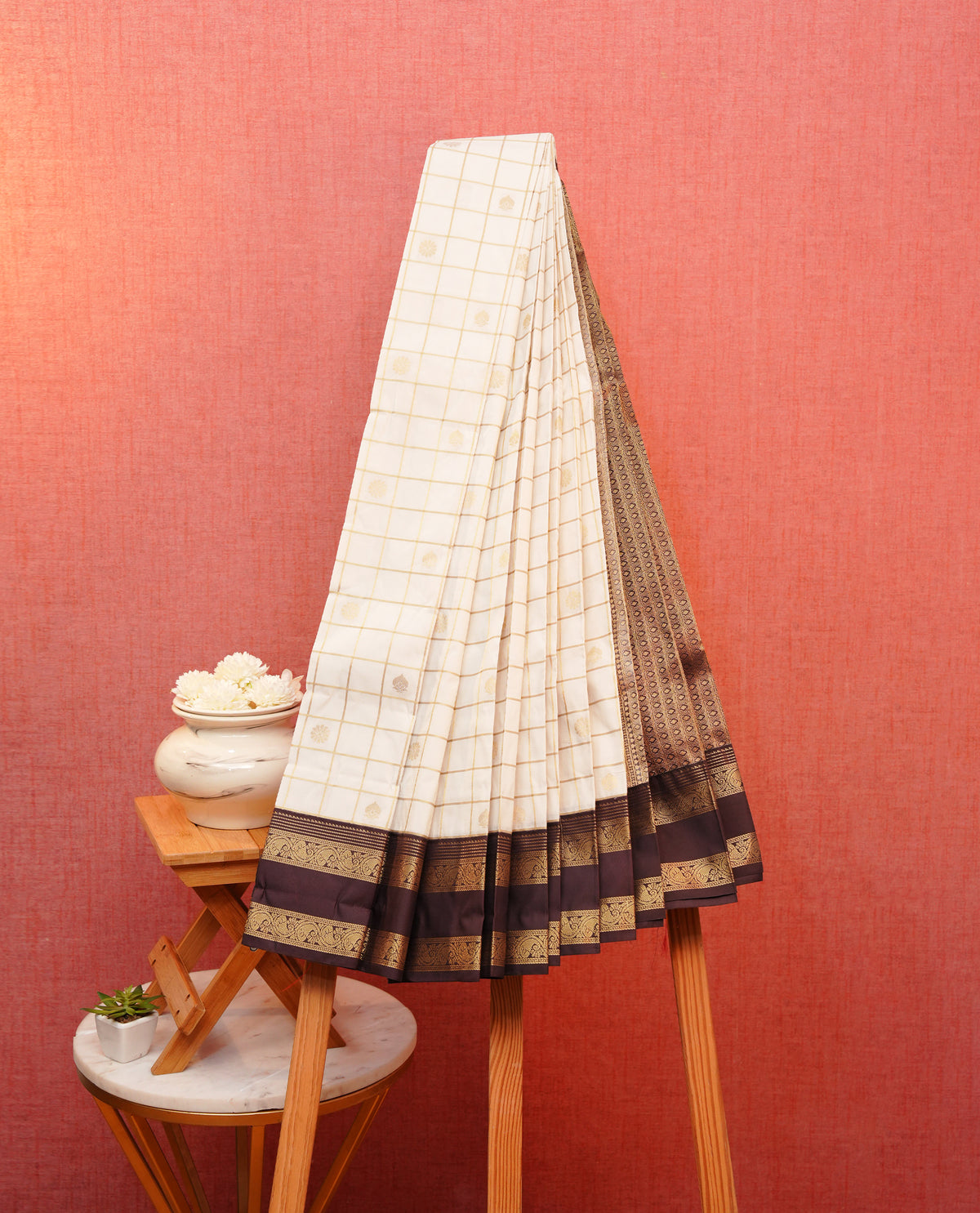 Cream colour soft silk saree featuring gold zari check pattern with floral mottifs on body, contrast dark brown colour gold zari traditional border, grand pallu comes with matching blouse piece.