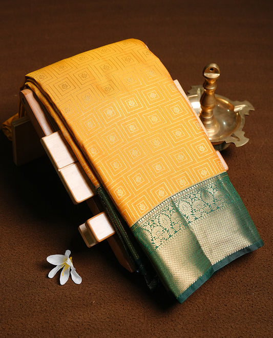 Mustard colour semi wedding saree featuring gold zari motif on check pattern on body, complemented by contrast green with traditional border, paired with matching blouse piece.