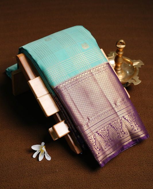 Light aqua colour semi wedding saree featuring gold zari motif on check pattern on body, complemented by contrast purple with traditional border, paired with matching blouse piece.