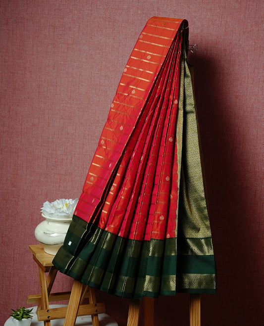 Rust orange coloured soft silk saree featuring gold zari stripes and motifs across the body, enhanced with a contrast Green border and pallu, paired with a matching contrast blouse piece.
