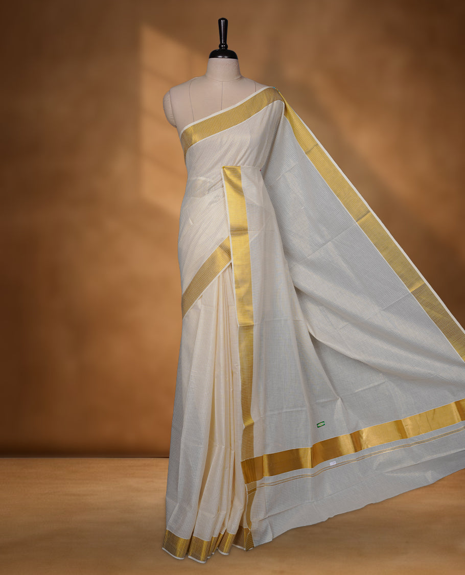 Off-white colour cotton Kerala saree featuring a traditional gold kasavu border with a fine striped texture across the body and pallu, offering a clean, elegant look, and paired with a matching blouse.
