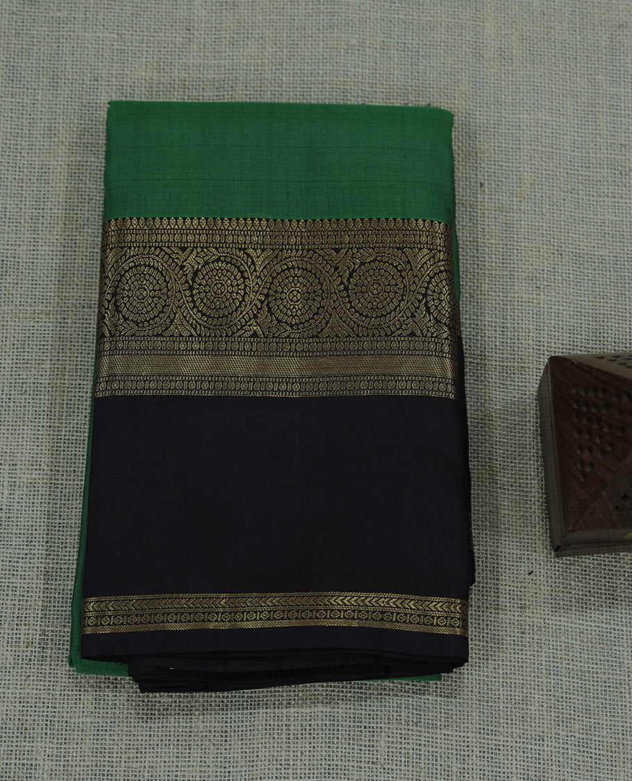 Green and Brown colour soft silk saree featuring a rich green body contrasted with a black pallu and intricate gold zari border.