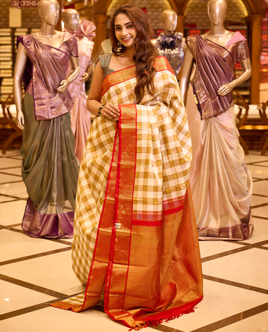 Graceful deep brown colour Kancheepuram silk saree featuring an intricate check pattern with peacock and chakram motifs woven across the body, beautifully enhanced with a rich red hued gold zari border, paired with a matching blouse piece.