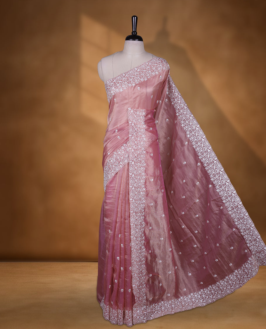 Pink colour net organza designer saree featuring a subtle self patterned body and an intricately scalloped floral thread embroidered border all around, complemented by a coordinating embroidered pallu and paired with a matching blouse.