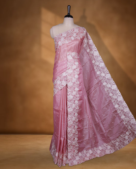 Pink colour organza designer saree featuring a subtle self patterned body and an intricately scalloped floral thread embroidered border all around, complemented by a coordinating embroidered pallu and paired with a matching blouse.