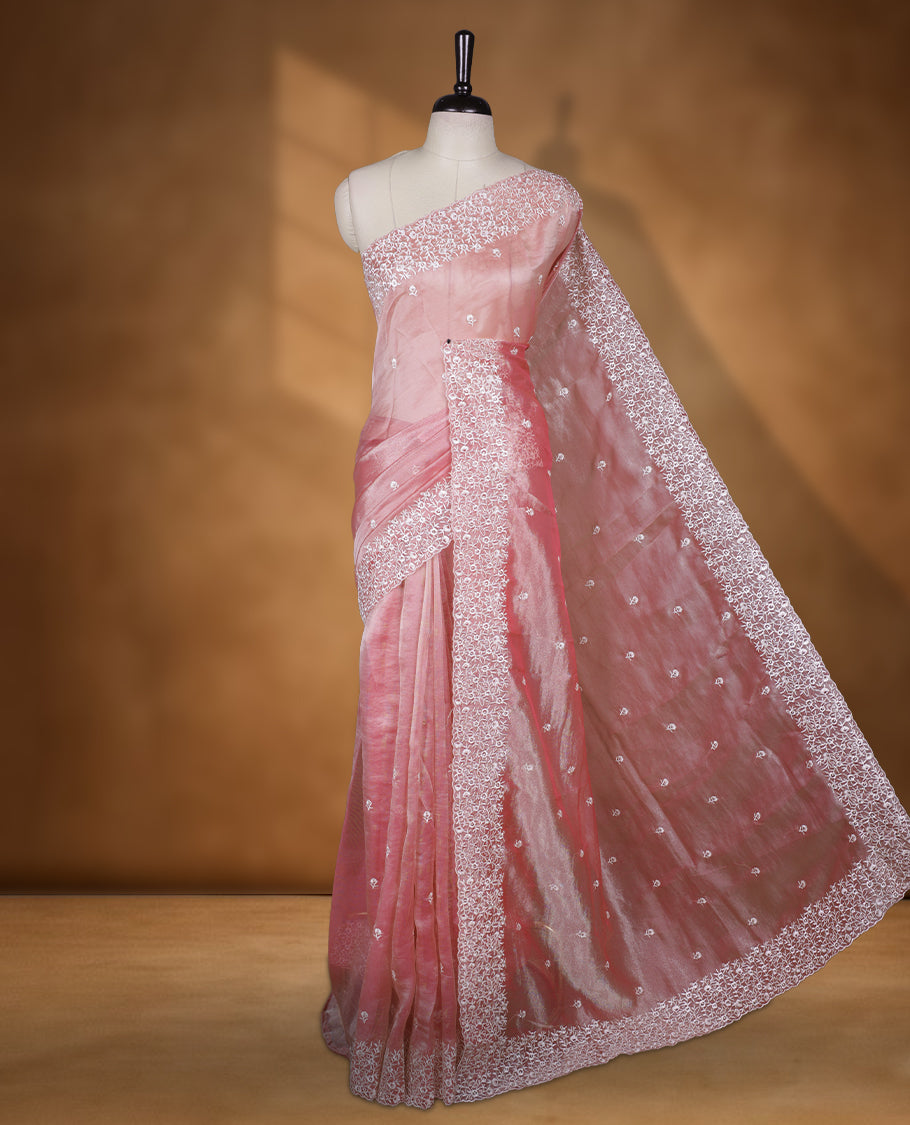 Peach colour net organza designer saree featuring a subtle self patterned body and an intricately scalloped floral thread embroidered border all around, complemented by a coordinating embroidered pallu and paired with a matching blouse.