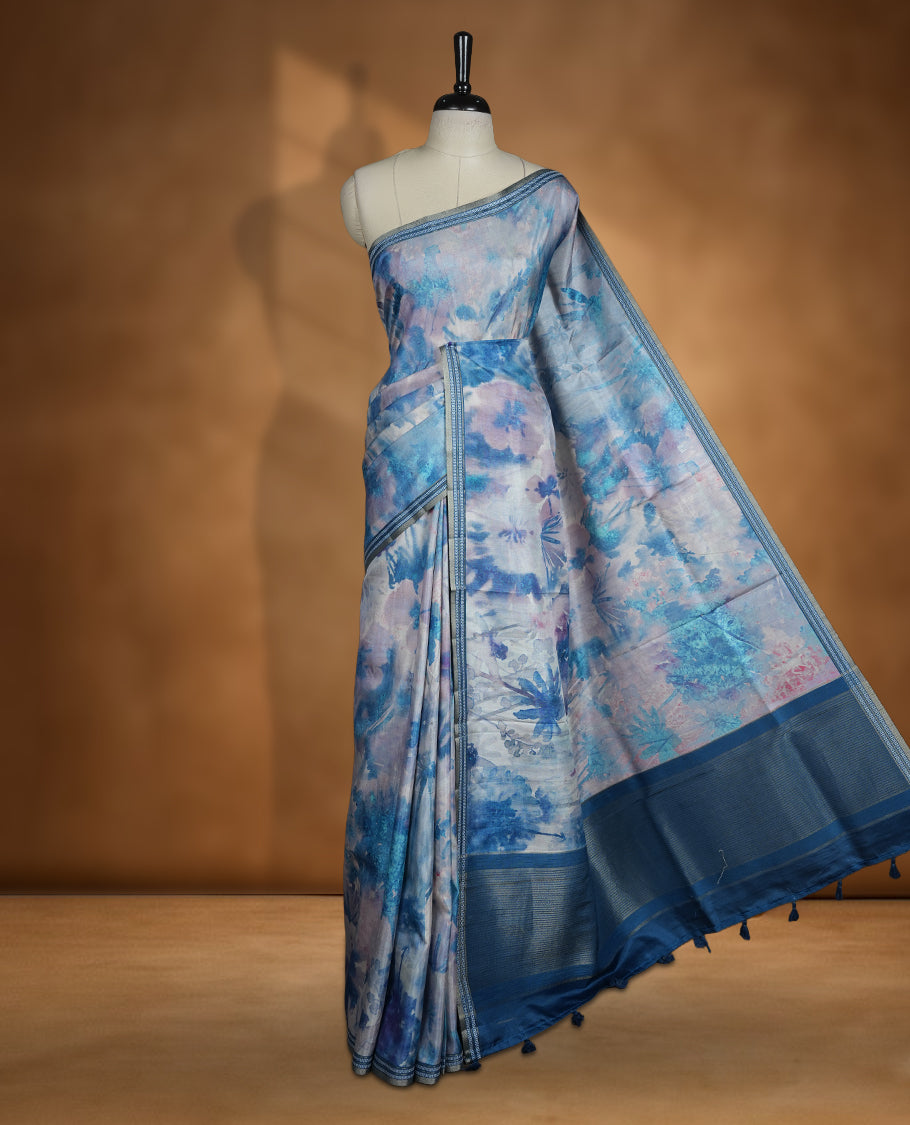 Sky blue colour semi tussar silk saree featuring a dreamy abstract digital floral printed body, finished with a rich self border and tasselled pallu, paired with a matching blouse.