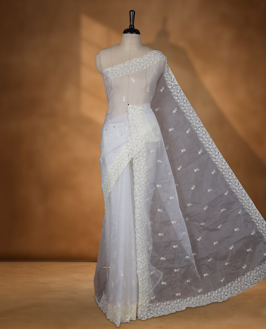 Light yellow colour organza designer saree featuring a subtle self patterned body and an intricately scalloped floral thread embroidered border all around, complemented by a coordinating embroidered pallu and paired with a matching blouse.