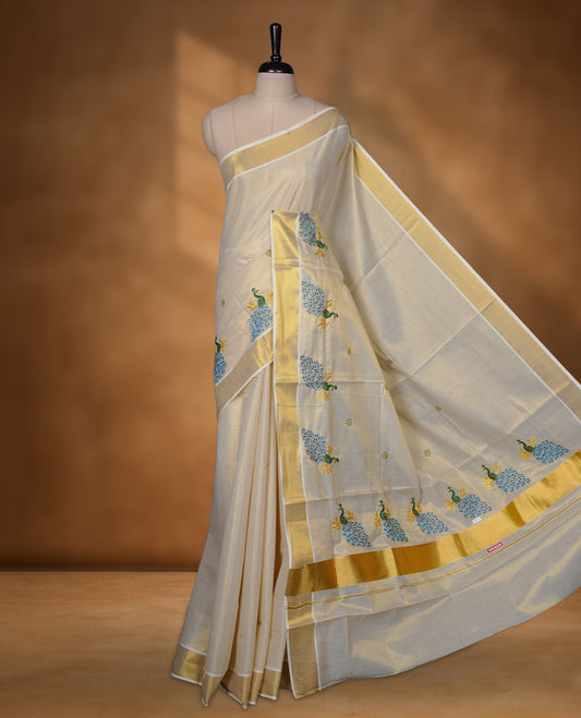 Off-white Kerala saree featuring a classic gold kasavu border, highlighted with graceful blue peacock motifs across the body and pallu, and paired with a matching blouse.
