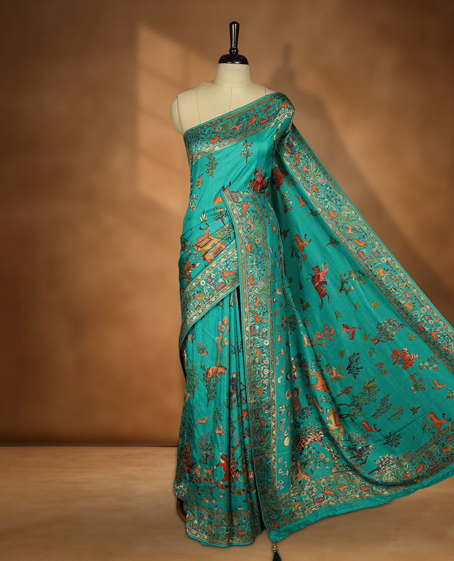 Turquoise sea green colour Pashmina silk saree lavishly adorned with all‑over woven wildlife and forest motifs, framed by an intricately detailed animal & floral zari border and grand storytelling pallu, paired with a matching woven border blouse piece.
