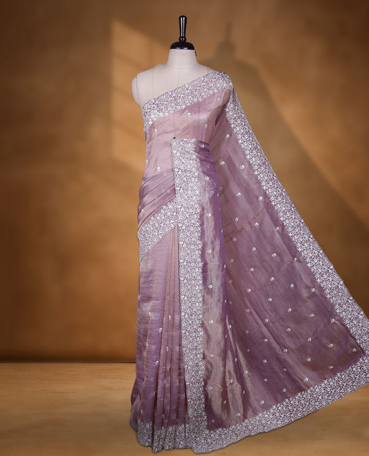 Light purple colour net organza designer saree featuring a subtle self patterned body and an intricately scalloped floral thread embroidered border all around, complemented by a coordinating embroidered pallu and paired with a matching blouse.
