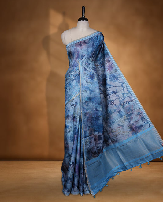 Ocean blue colour semi tussar silk saree featuring an abstract floral printed body with a rich self border and tasselled pallu, paired with a matching blouse.