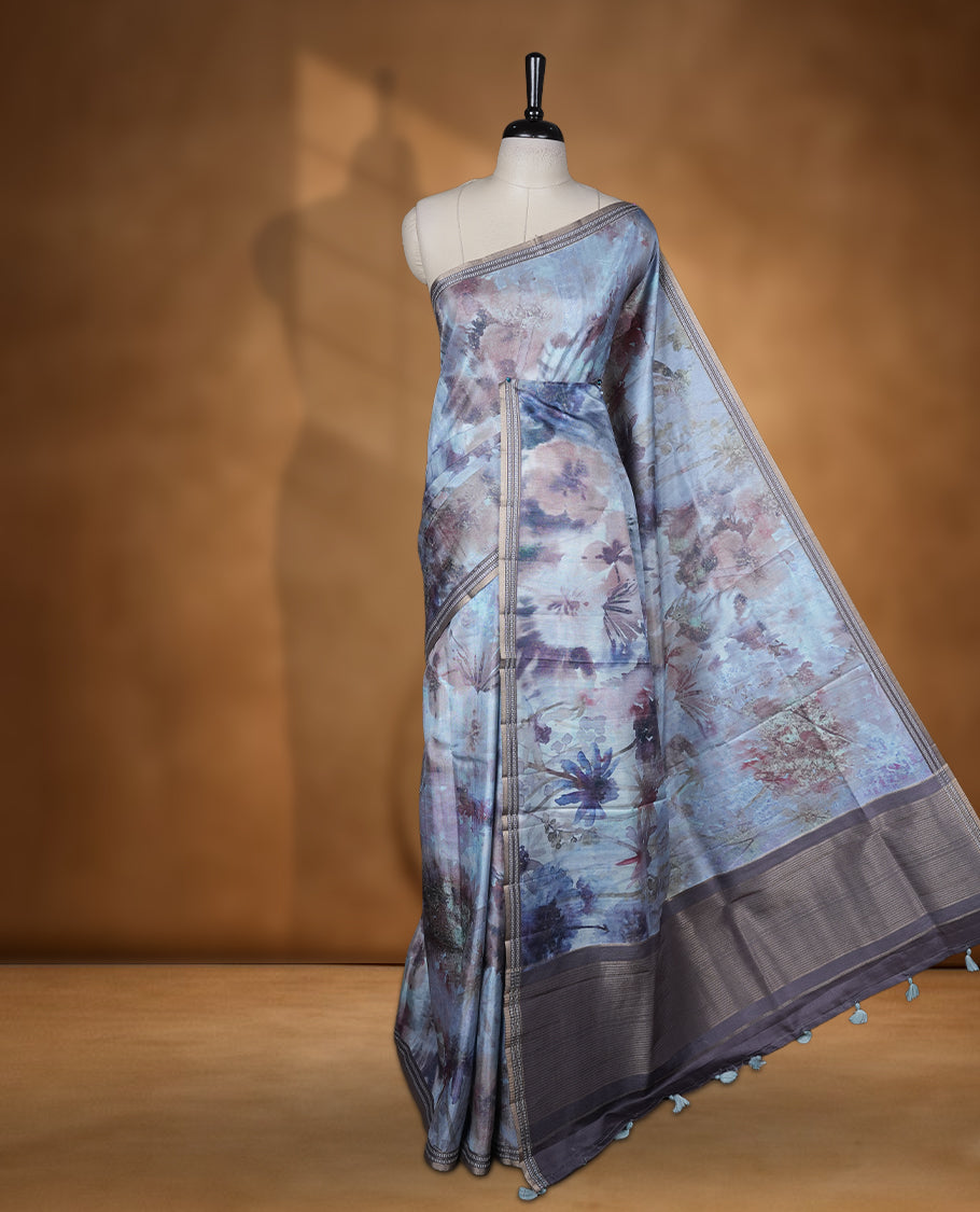 Smoky grey colour semi tussar silk saree featuring an abstract digital floral printed body, finished with a rich self border and tasselled pallu, paired with a matching blouse.