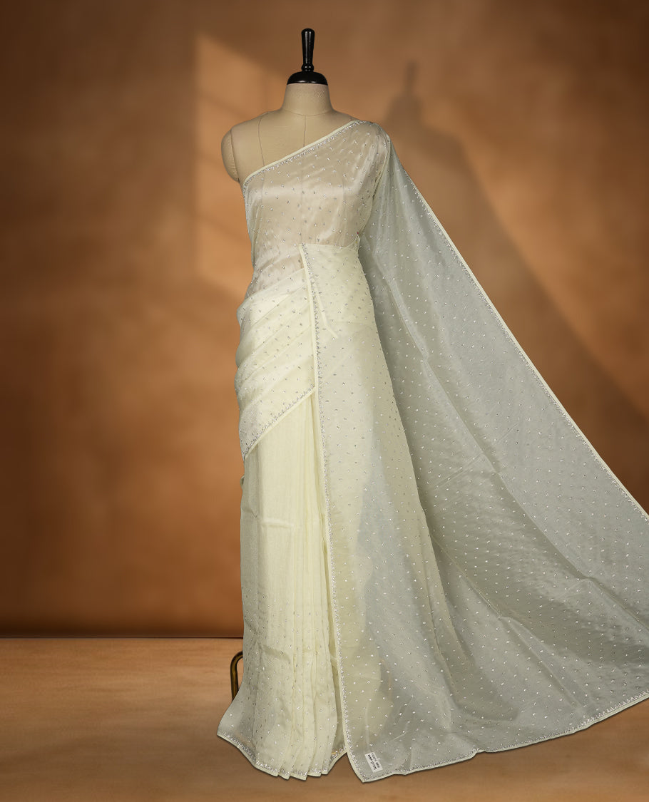 Cream Colour net shimmer fancy saree adorned with white stone buttas all over the body, paired with a delicate stone worked border and matching blouse